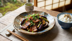 A appetizing plate of Japanese-style miso stir-fried sliced pork belly, soft eggplant, and scallions coated in a caramelized miso sauce, served on a ceramic plate alongside a bowl of steamed white rice on a rustic wooden table.