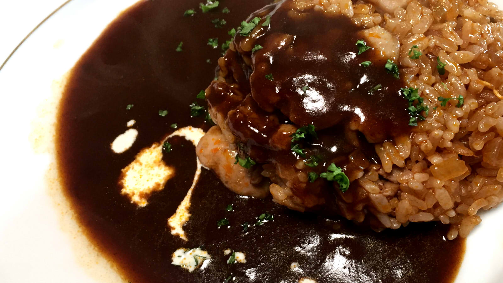 Silky rich dark Japanese demiglace sauce poured over omurice in a pan