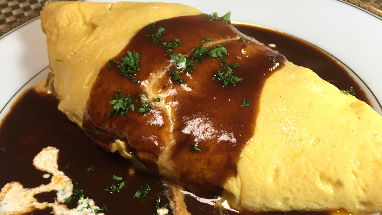 Authentic Japanese Omurice wrapped in soft egg topped with demiglace sauce and fresh cream