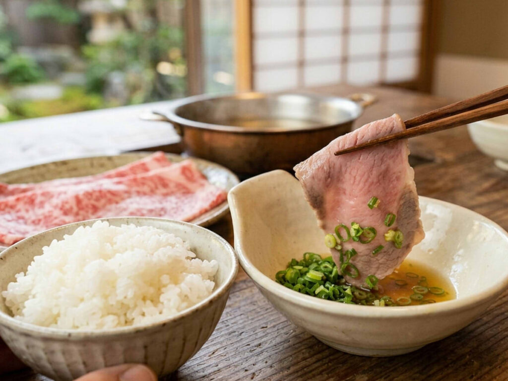 A close-up point-of-view shot of Japanese shabu-shabu dining. Chopsticks hold a tender, thinly sliced Wagyu beef cooked to a delicate pink, dipping it into a small bowl of citrus ponzu sauce topped with finely sliced green onions (uchi-negi). On the lower left, a hand holds a bowl of fluffy, freshly steamed white rice. Raw marbled beef slices and a copper hot pot are visible in the background.
