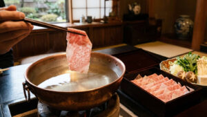 Thinly sliced Wagyu beef held by chopsticks over a simmering copper hot pot